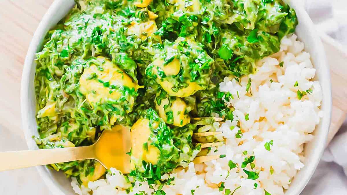 A bowl of white rice topped with a creamy green spinach and cheese mixture, garnished with chopped herbs, and a fork resting inside the bowl.