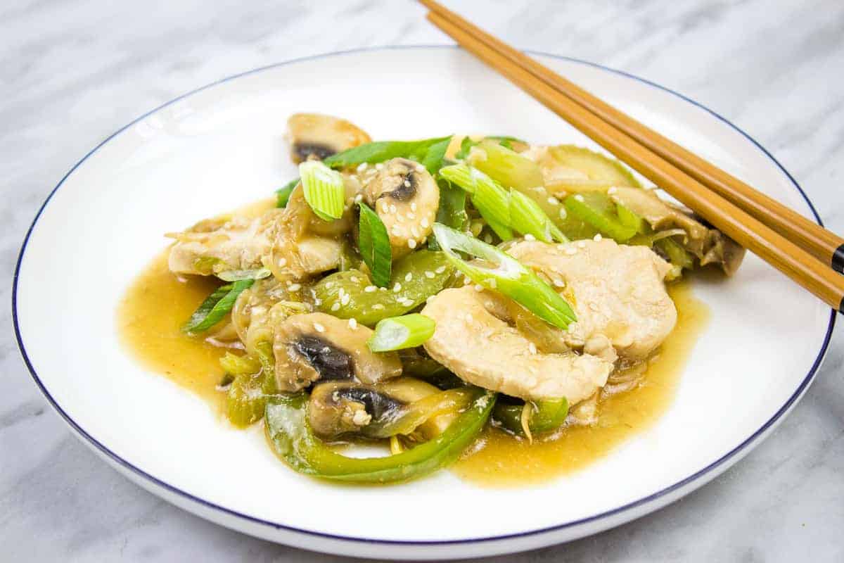 A plate of stir-fried chicken with mushrooms, green bell peppers, and scallions in a brown sauce, served with chopsticks on a white plate.