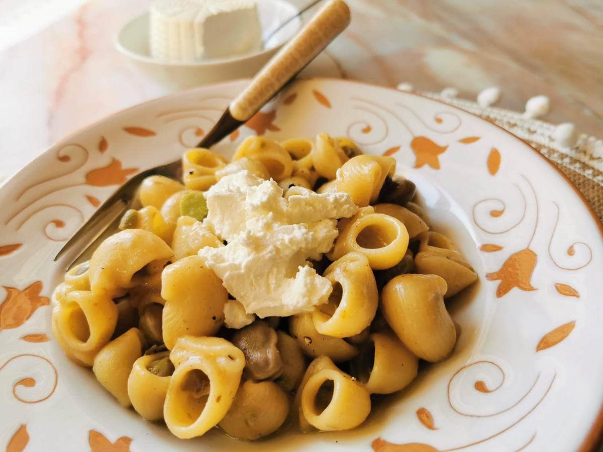 A plate of pasta with mushrooms and green vegetables, topped with a dollop of ricotta cheese, with a fork resting on the plate.