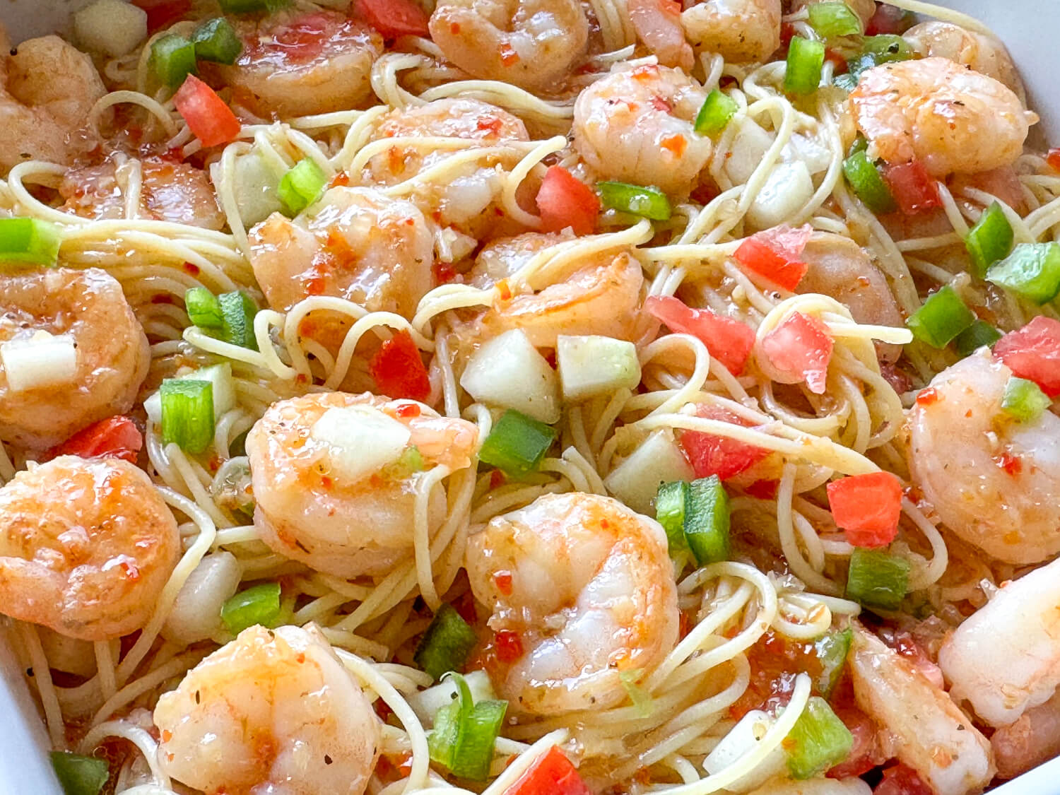 Cooked shrimp, spaghetti noodles, chopped green bell peppers, tomatoes, and onions mixed together in a light sauce.