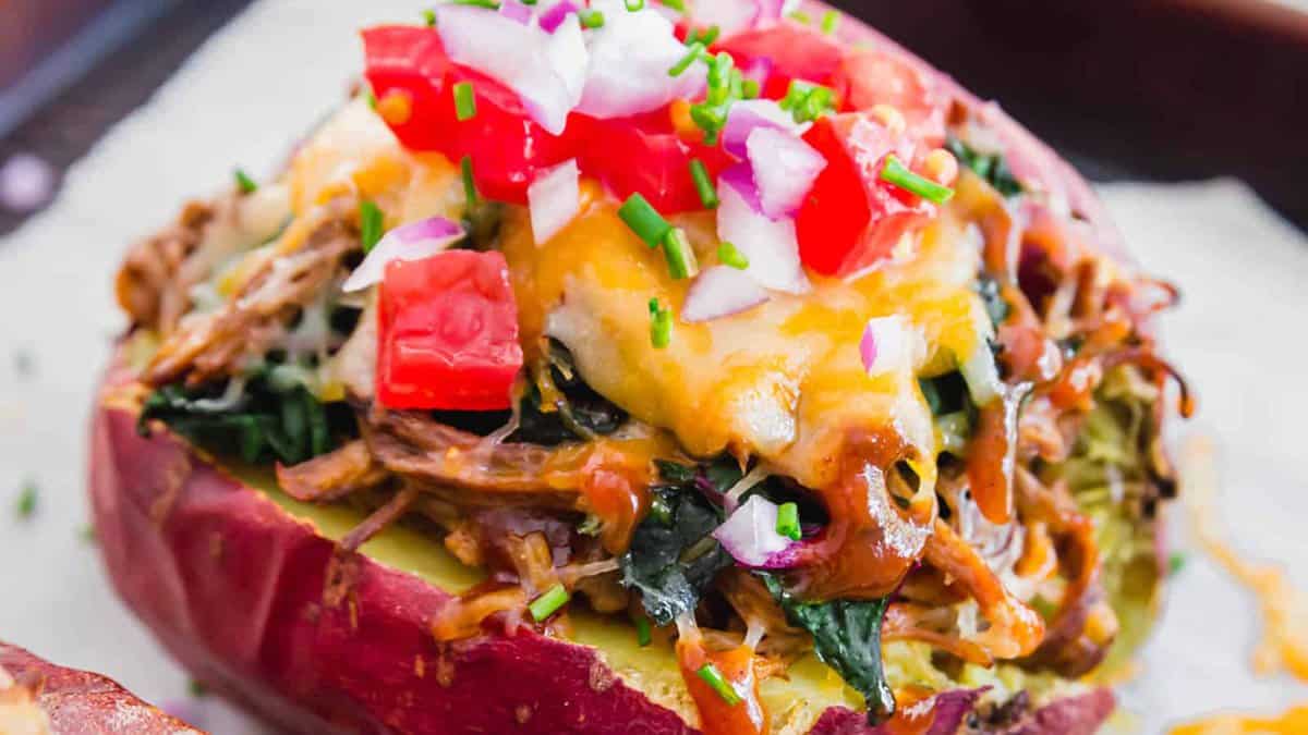 A baked sweet potato topped with shredded meat, melted cheese, chopped tomatoes, red onions, and chives.