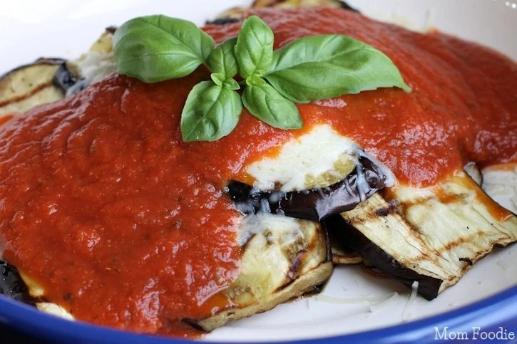 Slices of roasted eggplant topped with melted cheese, marinara sauce, and fresh basil leaves on a white plate.