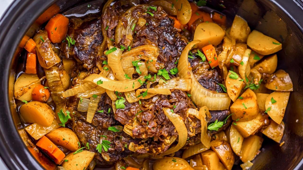A slow cooker pot roast with beef, sliced onions, carrots, and potatoes, garnished with chopped parsley.