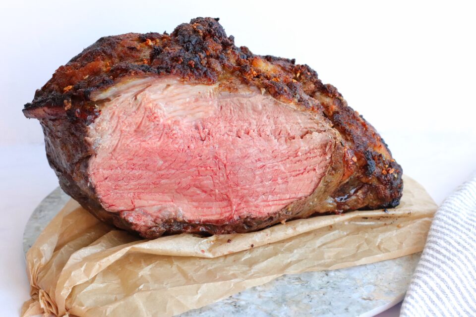 A cooked roast beef with a browned crust and a pink, medium-rare center, resting on parchment paper atop a marble surface.