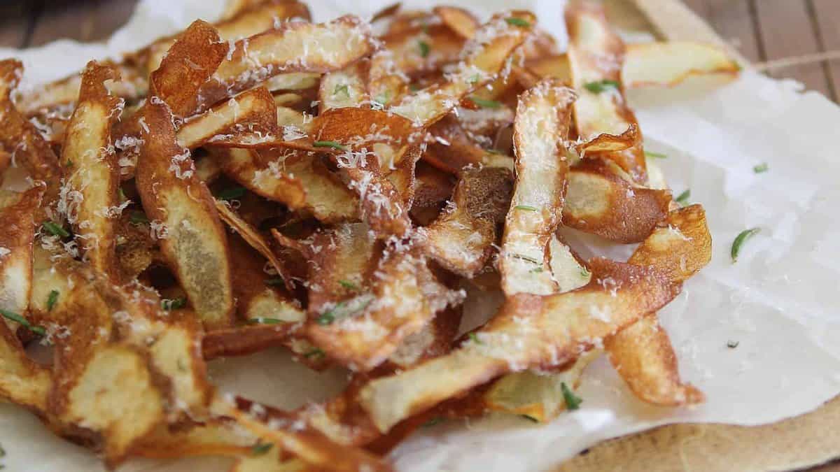 A pile of crispy potato peels garnished with grated cheese and herbs sits on a piece of parchment paper.