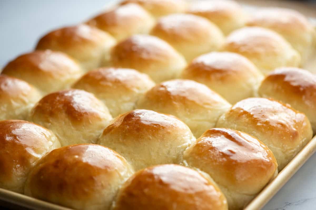 A baking tray filled with rows of golden-brown, freshly baked dinner rolls.