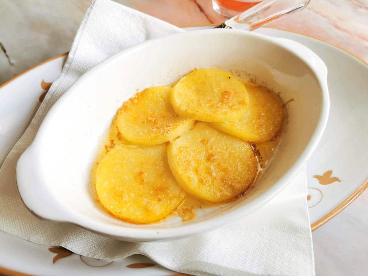 A white dish containing four golden-brown potato slices, arranged on a napkin atop a plate.