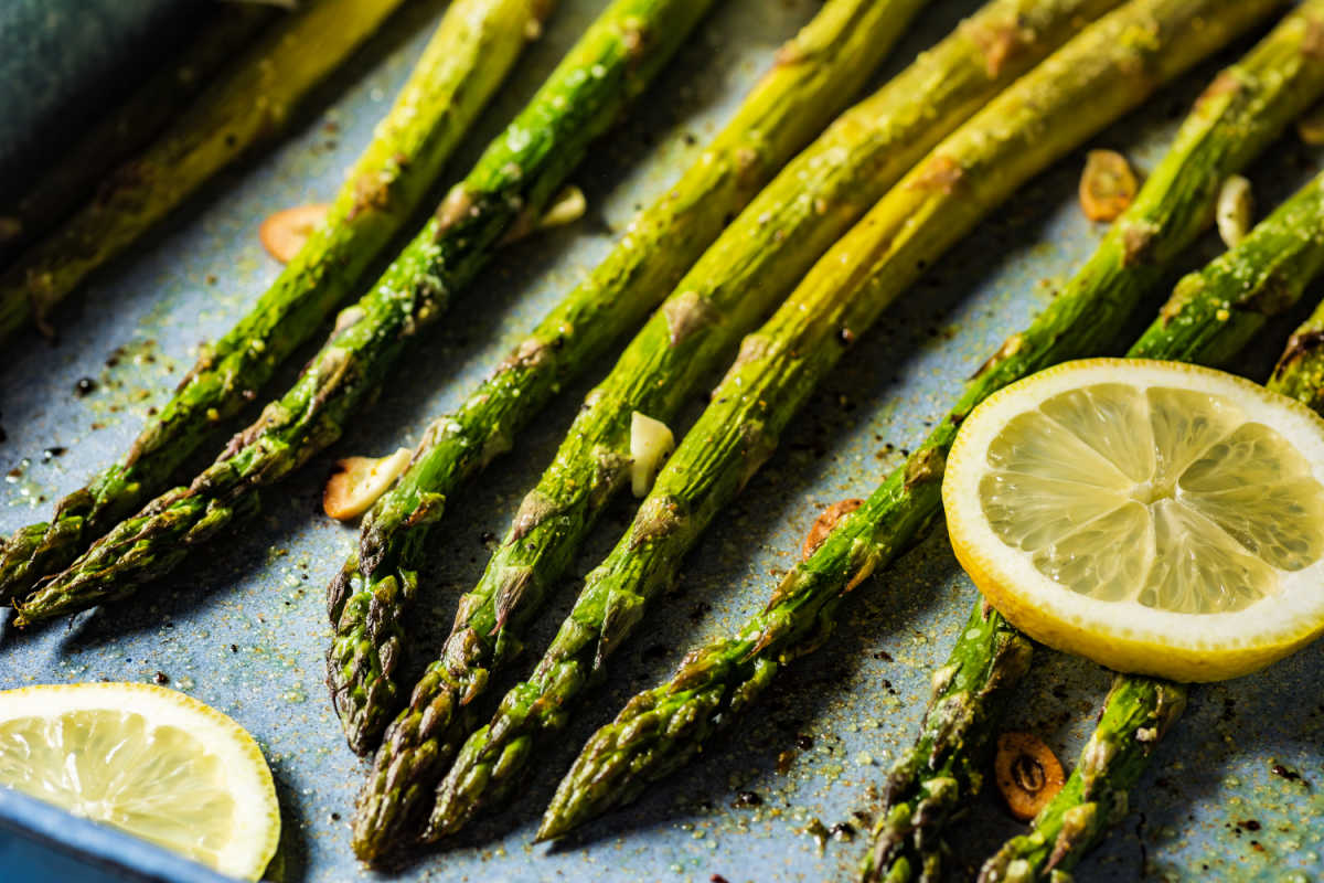 Roasted asparagus spears on a baking sheet, garnished with sliced garlic and lemon rounds.