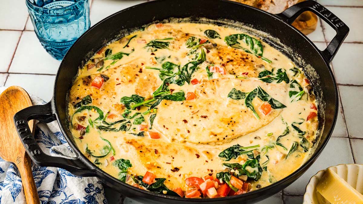 Creamy chicken breasts cooked in a skillet with spinach, diced tomatoes, and a rich white sauce.