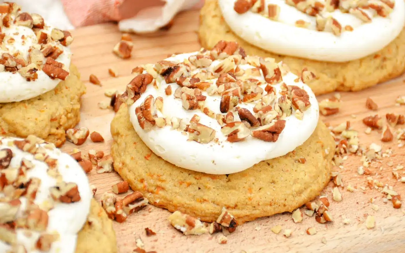 A close-up of cookies with a swirl of white frosting on top, sprinkled with chopped pecans, placed on a wooden surface.