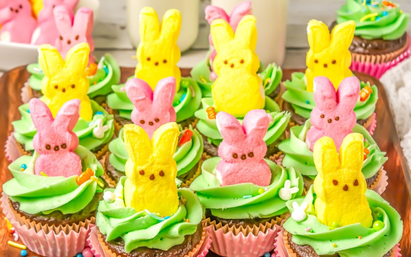 Cupcakes topped with green frosting and decorated with pink and yellow marshmallow bunny candies arranged on a tray.