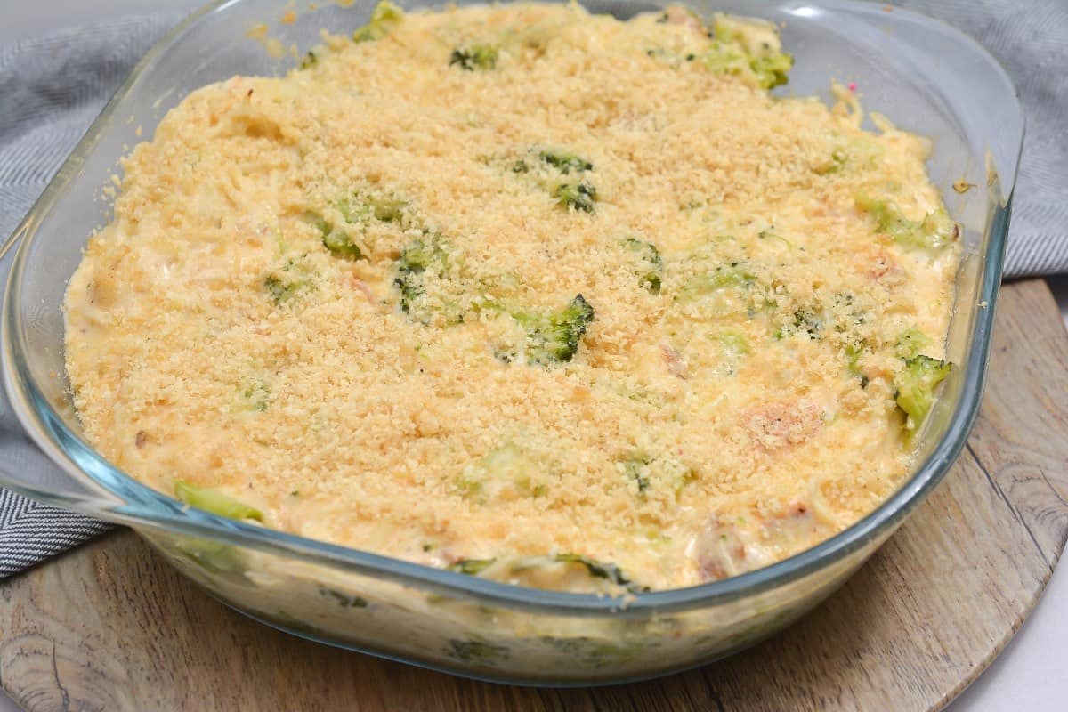 Glass baking dish filled with a creamy broccoli casserole topped with a layer of golden breadcrumbs, placed on a wooden surface.