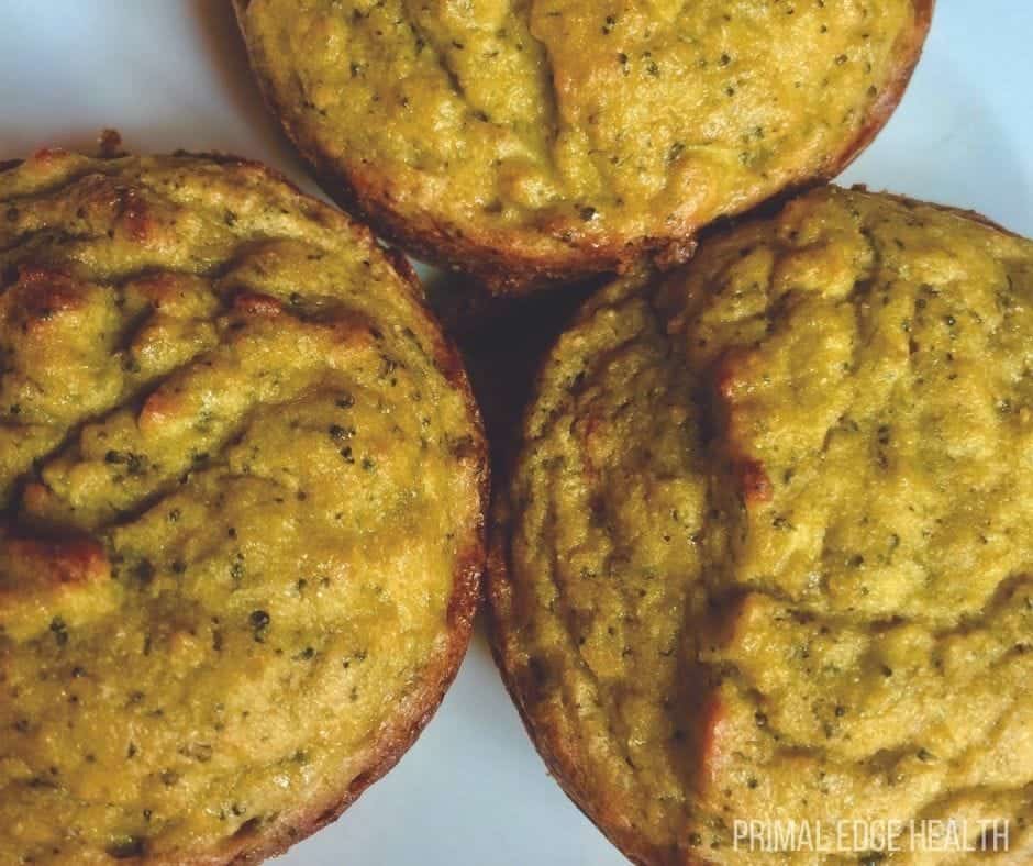 Three golden-brown muffins with visible green flecks sit on a white plate.