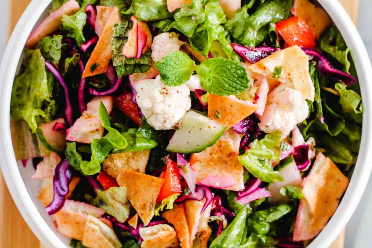 A bowl of fresh fattoush salad with lettuce, pita chips, cucumber, radish, red cabbage, cauliflower, and mint leaves.