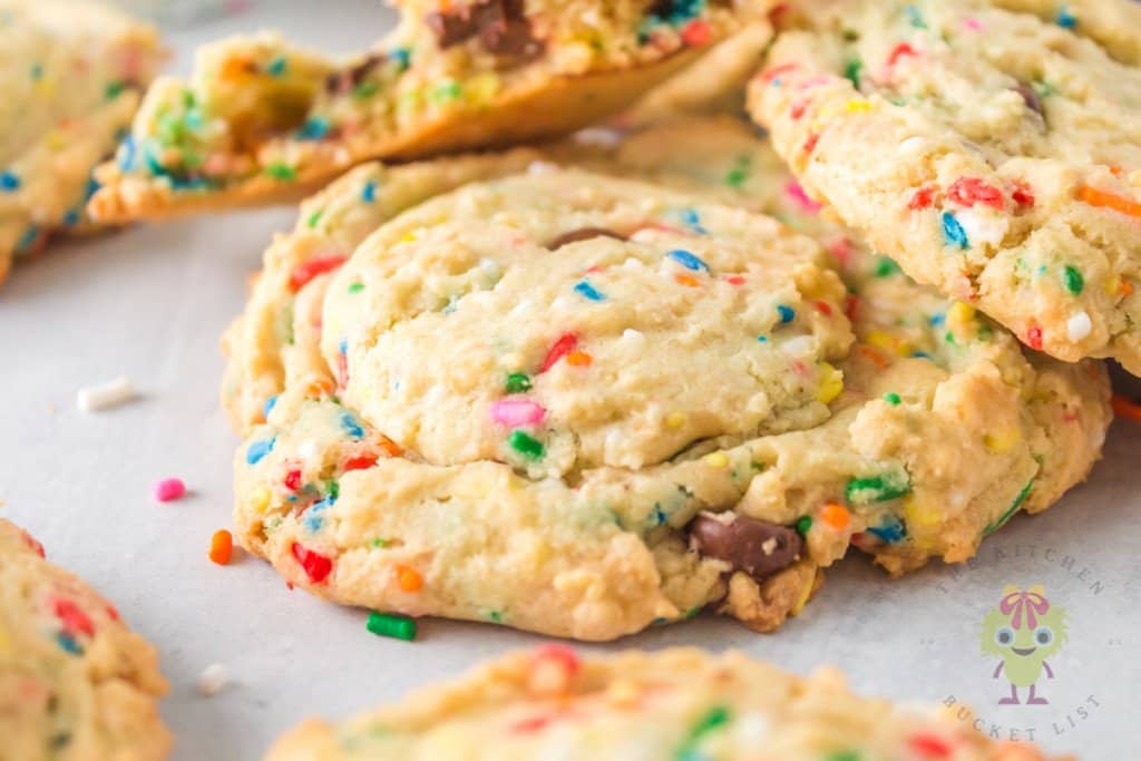 A close-up of several funfetti cookies with colorful sprinkles on a white surface.