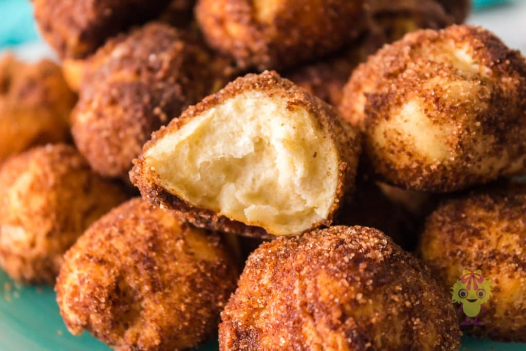 A close-up of several cinnamon sugar-coated dough balls, with one in the center broken open to show a soft, fluffy interior.
