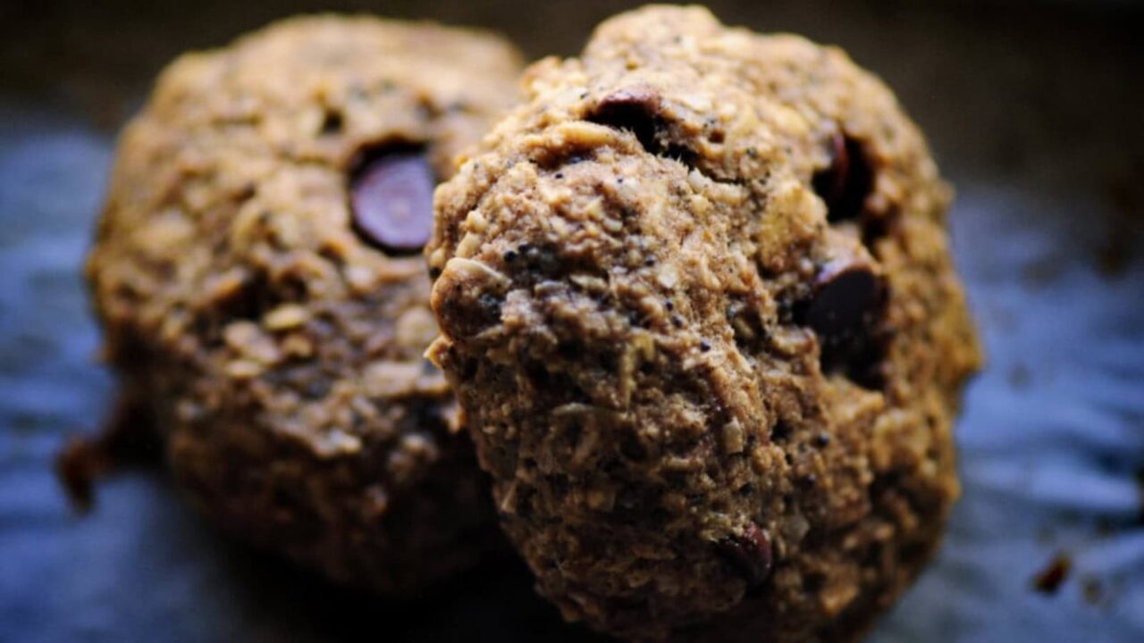 Two oatmeal chocolate chip cookies on a dark surface, shown in close-up.