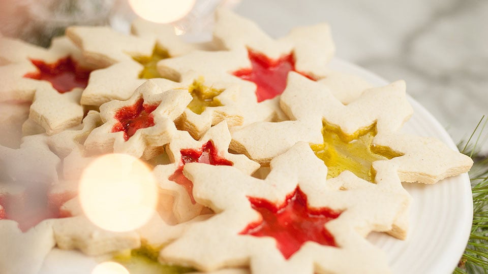 Plate of star-shaped sugar cookies with translucent, colored centers in red and yellow, arranged on a white surface.