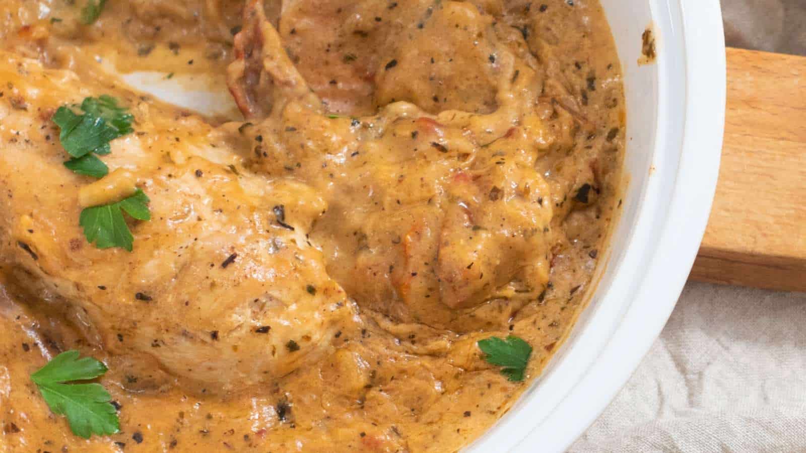 Chicken in a creamy, seasoned sauce garnished with parsley, served in a white dish.