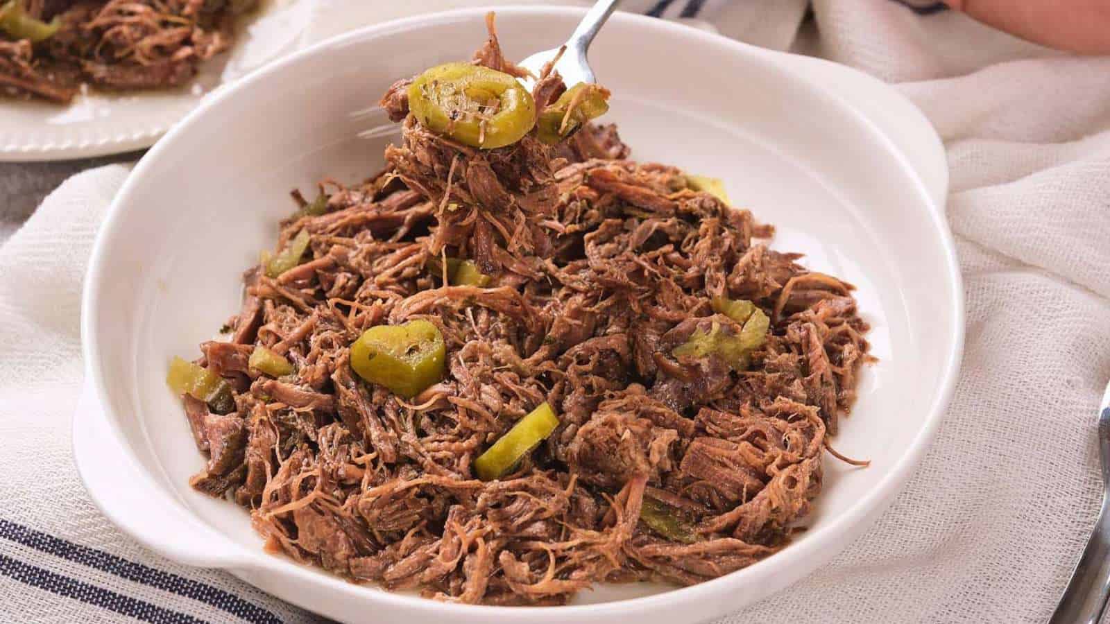 Shredded roast beef with sliced green peppers served in a white bowl, with a fork lifting a portion.