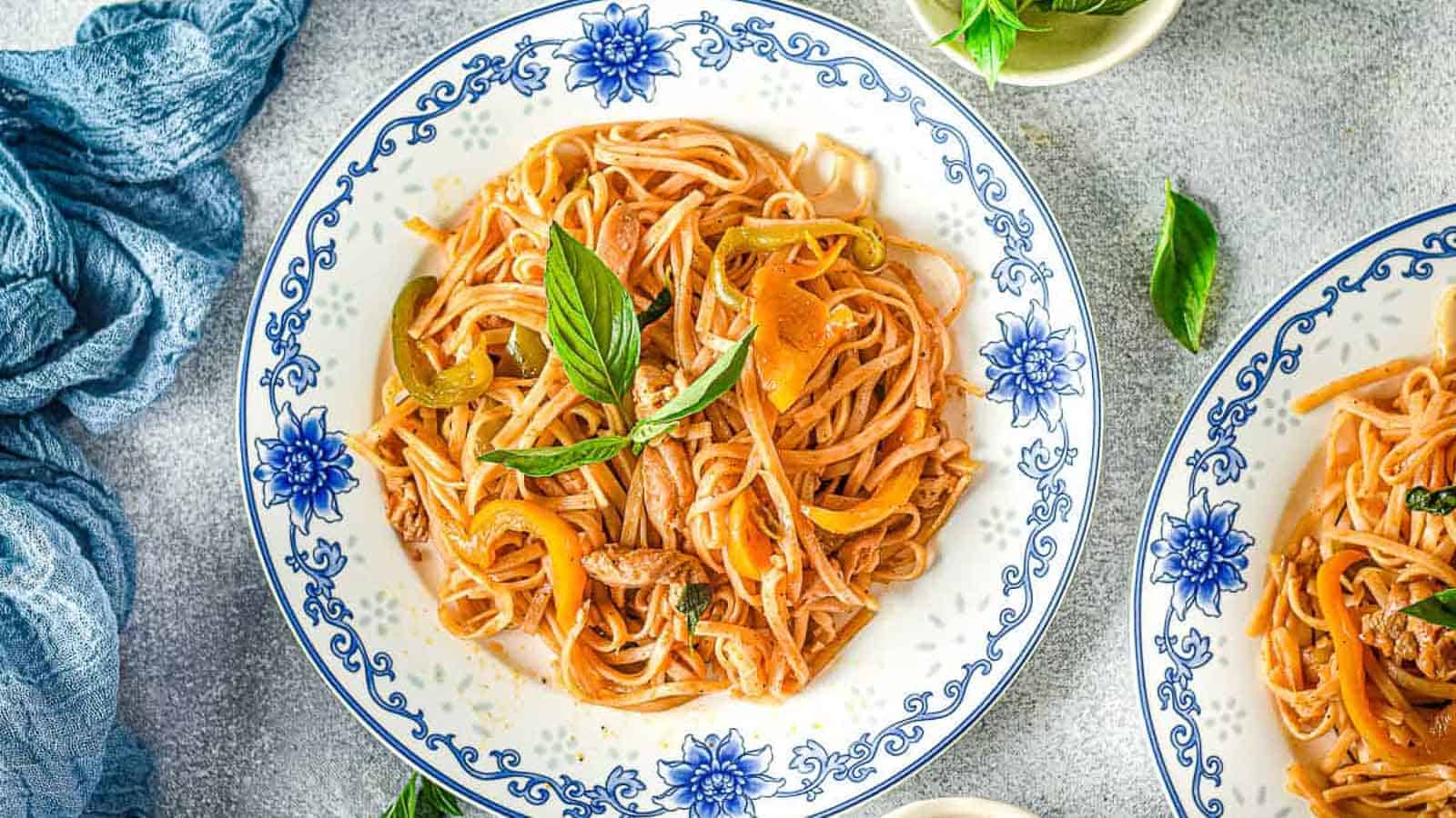 A plate of linguine pasta with tomato sauce, bell peppers, and fresh basil, served on a floral-patterned dish.