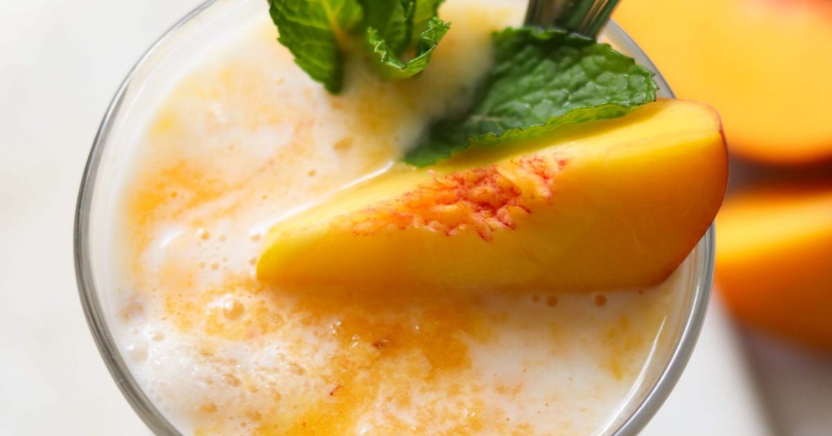A close-up of a creamy peach smoothie garnished with a peach slice and fresh mint leaves.
