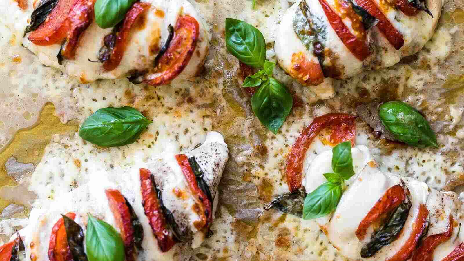 Baked chicken breasts stuffed with slices of tomato, mozzarella cheese, and basil, topped with melted cheese, on a parchment-lined tray.