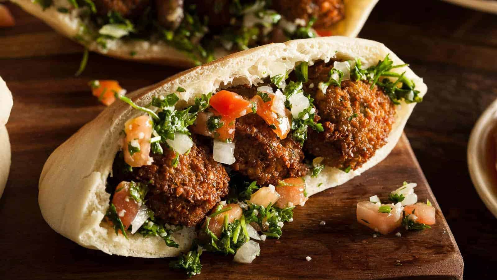 A pita bread filled with falafel balls, chopped tomatoes, onions, and parsley on a wooden surface.