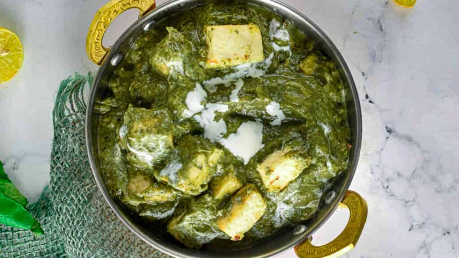 A bowl of palak paneer, featuring cubes of paneer cheese in a creamy spinach gravy, garnished with a swirl of cream.