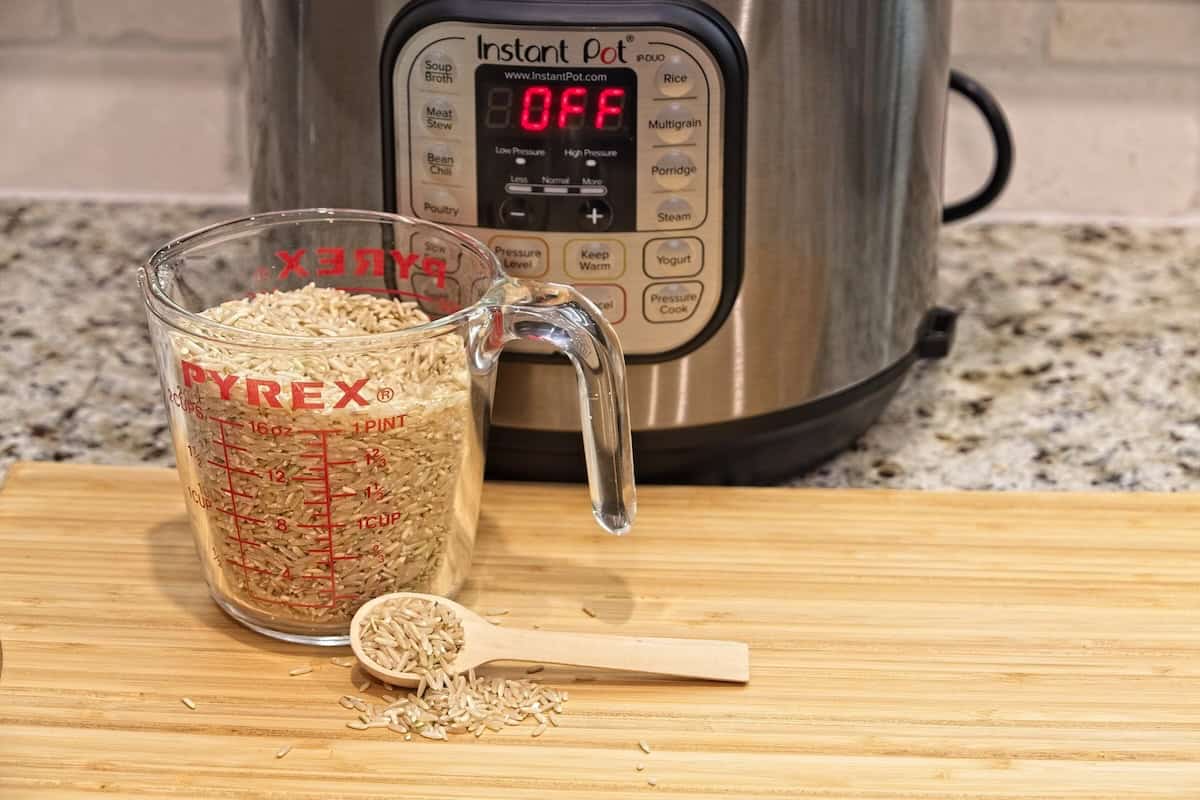 A glass measuring cup filled with dry rice and a wooden spoon rest on a cutting board in front of an Instant Pot with the display reading OFF.