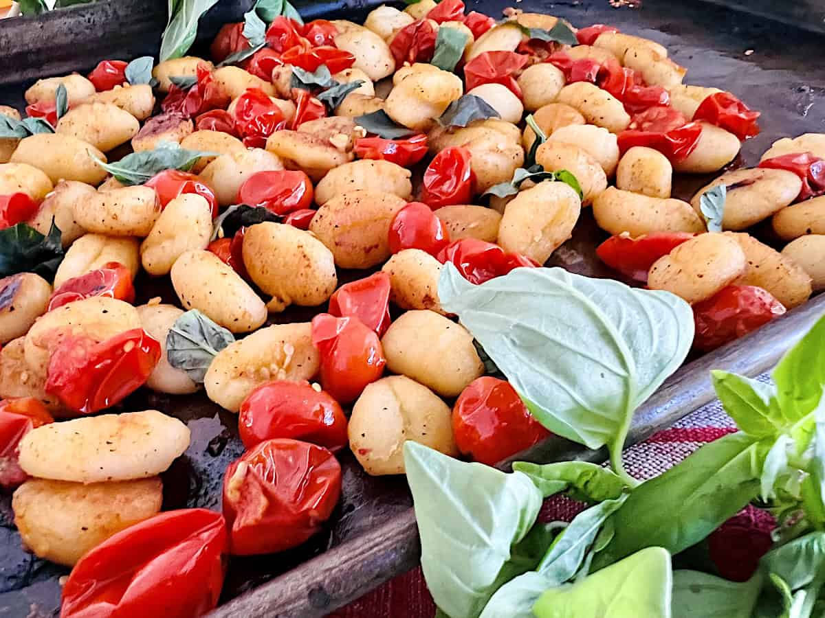 Pan of cooked gnocchi with roasted cherry tomatoes and fresh basil leaves scattered on top.