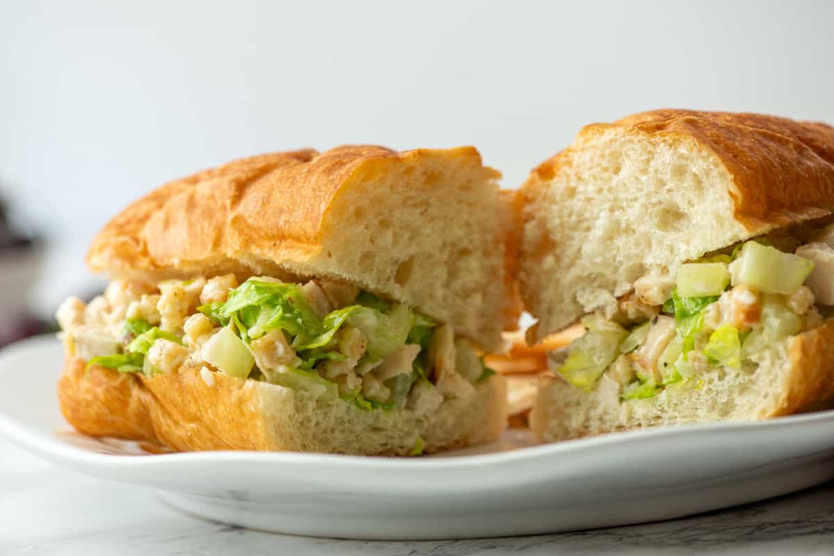 A croissant sandwich filled with chopped lettuce, chicken, and diced vegetables, cut in half and served on a white plate.