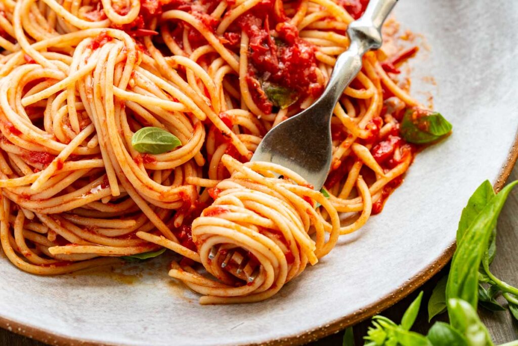 Plate of spaghetti with tomato sauce, garnished with basil leaves, and a fork twirling a portion of the pasta.