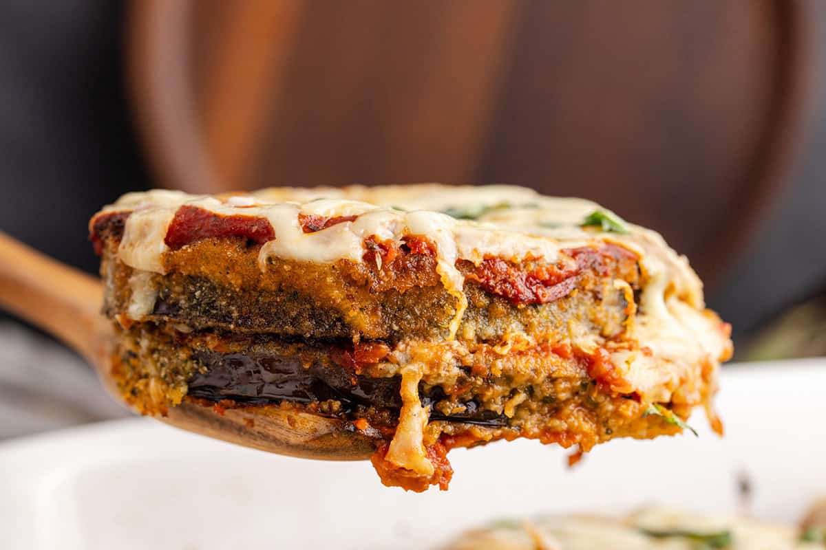 A close-up of a serving of eggplant parmesan on a wooden spoon, showing layers of breaded eggplant, tomato sauce, and melted cheese.