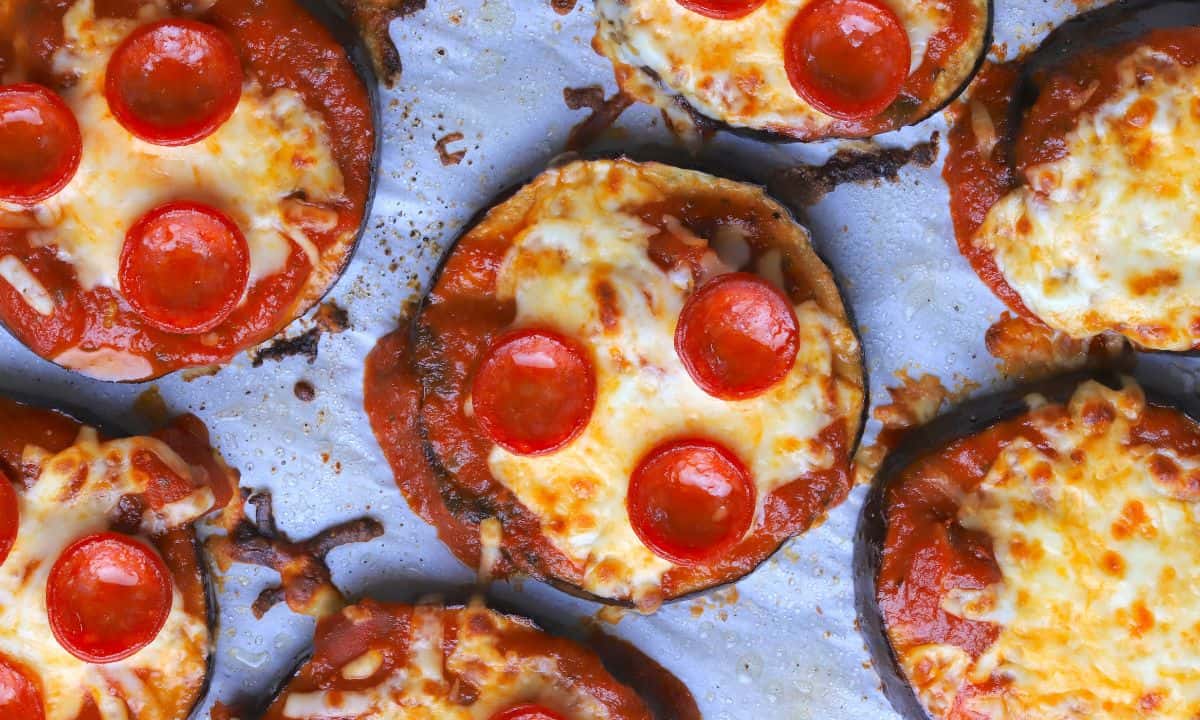 Mini pizzas topped with melted cheese and pepperoni slices are arranged on a baking sheet.