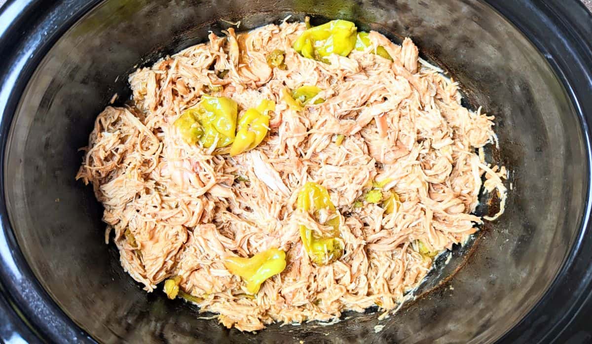 Shredded chicken with pepperoncini peppers in a slow cooker.