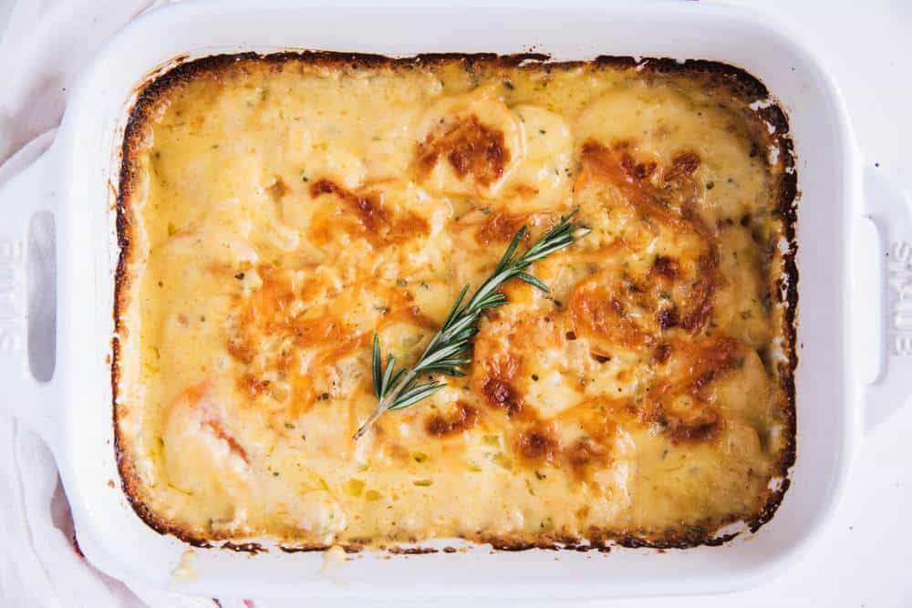 Baked cheesy potato gratin in a white rectangular dish, topped with a sprig of fresh rosemary.