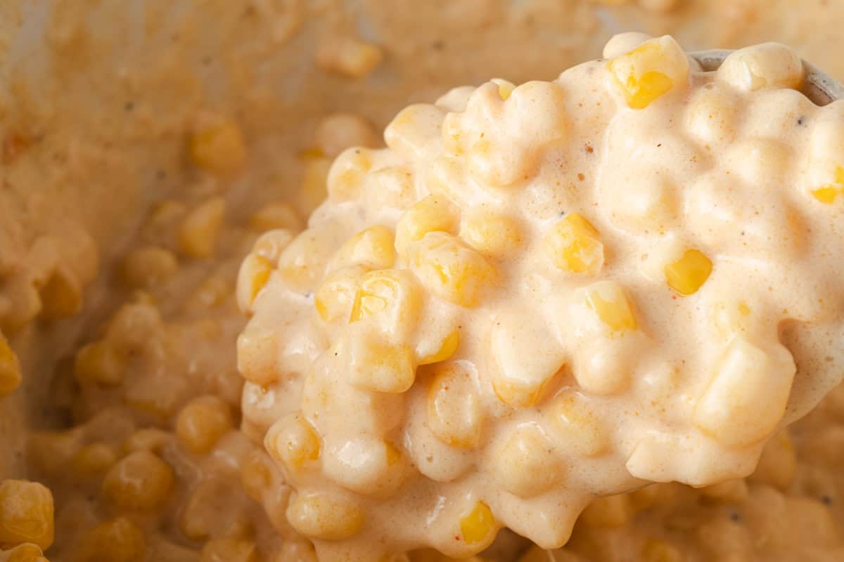 Close-up of creamy corn kernels in a thick, cheesy sauce, with a spoon lifting a portion from the mixture.
