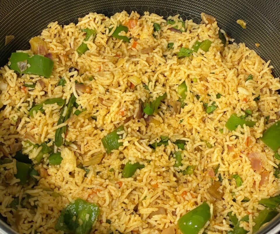 Close-up of cooked rice mixed with chopped green bell peppers, onions, and spices in a nonstick pan.