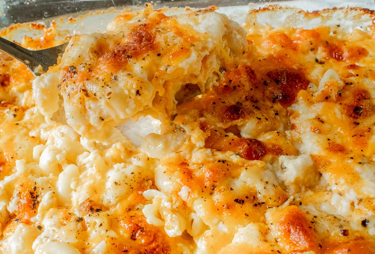 A close-up of baked macaroni and cheese being served from a casserole dish, showing melted cheese and browned, crispy edges.
