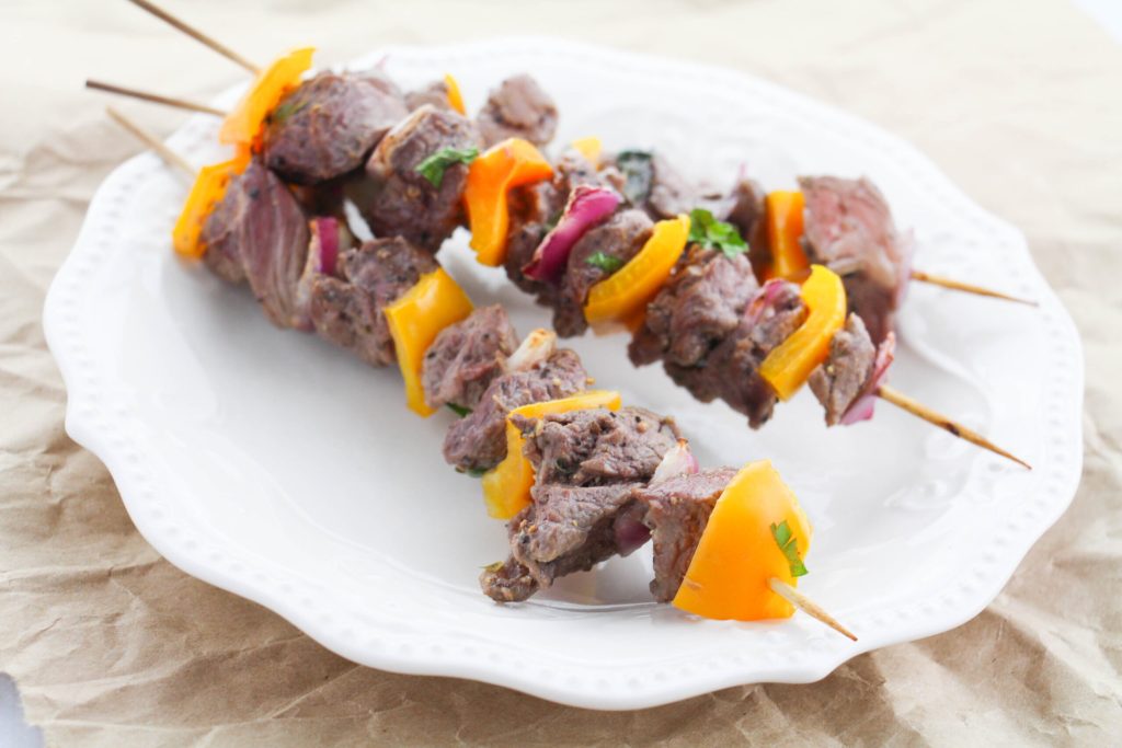Three beef and vegetable skewers with yellow bell peppers and red onions on a white plate.