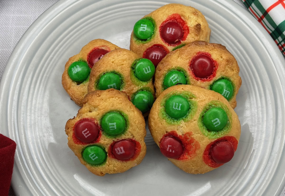A plate with six cookies topped with red and green M&M candies arranged on a white plate.