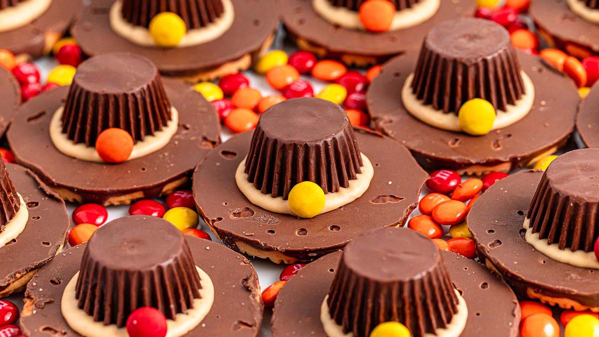 Chocolate candy hats made from peanut butter cups, chocolate cookies, and colorful candy pieces, arranged on a bed of small round candies.