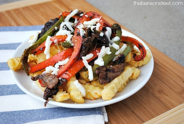 Crinkle-cut fries topped with sautéed beef, red and green bell peppers, and melted cheese on a white plate.