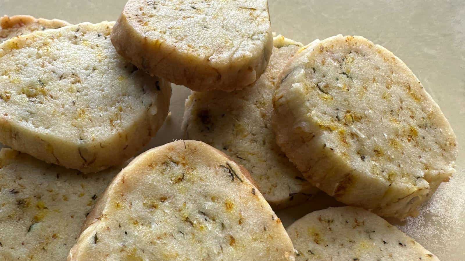 A close-up of several round, sliced shortbread cookies with visible flecks of herbs and zest on a light surface.