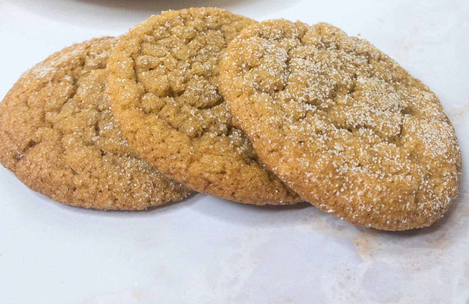 Three round, sugar-coated cookies are arranged overlapping each other on a light-colored surface.