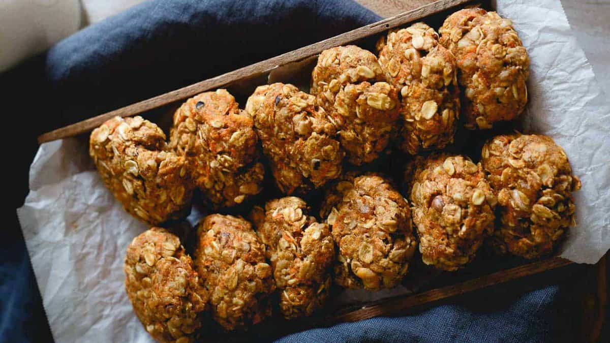A wooden tray lined with parchment paper holds a row of homemade oatmeal cookies with visible oats and nuts.