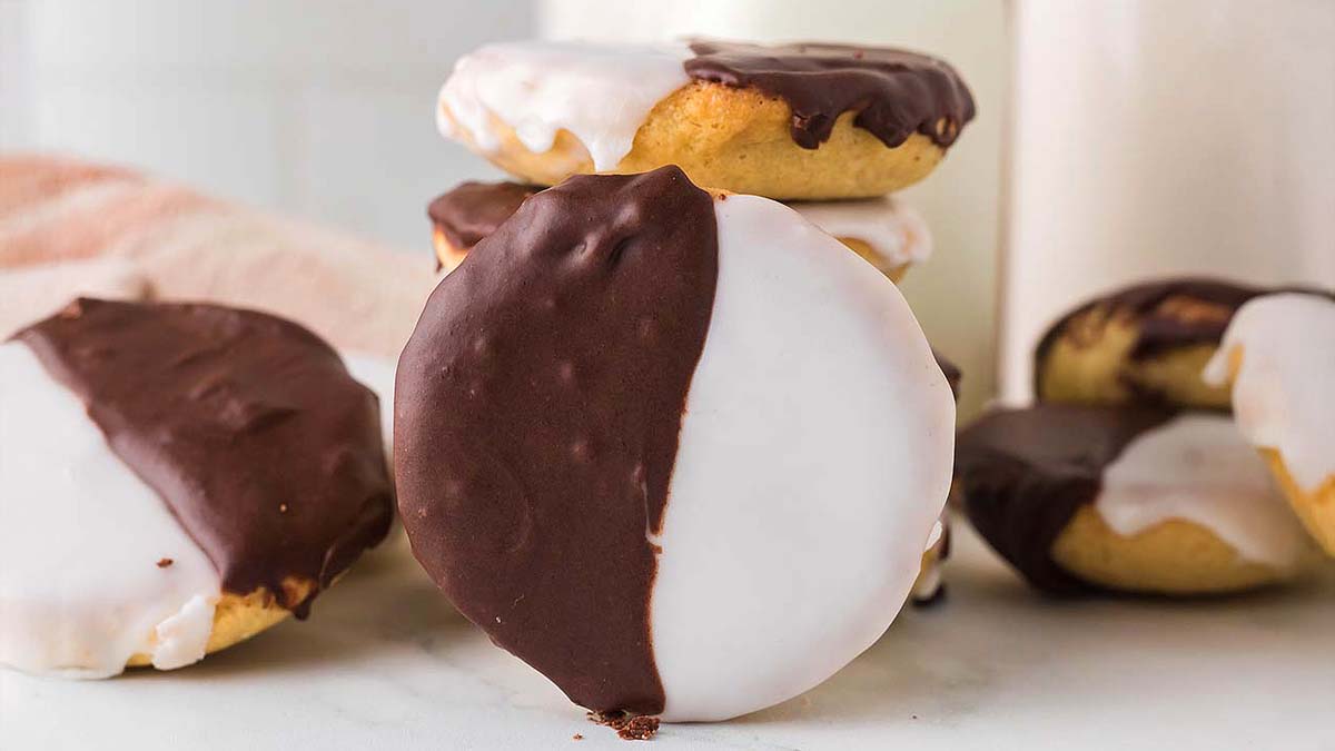 Several black and white cookies are stacked and arranged on a white surface, each half-covered in chocolate icing and half in white icing.