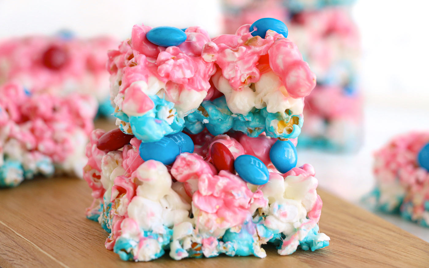 Two colorful popcorn bars with pink and blue melted coating and red and blue chocolate candies stacked on a wooden surface.