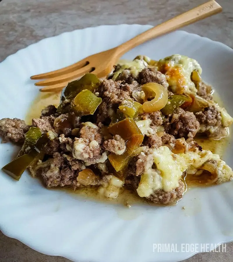 A serving of ground beef, green bell peppers, onions, and melted cheese on a white plate with a wooden fork.